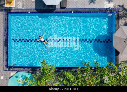 Junge Frau in weißem Badeanzug, entspannend im Schwimmbad der luxuriösen Villa. Draufsicht aus der Luft. Unachtsames Sommerurlaubskonzept. Stockfoto