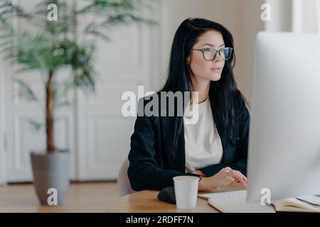 Seriöse Geschäftsfrau, elegant im Teamarbeitsbereich, konzentriert sich auf Überwachung, Kaffee trinken, Daten analysieren. Stockfoto