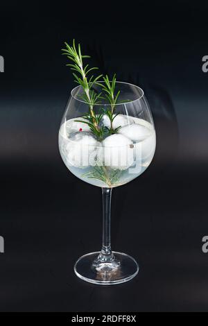Gin-Tonic-Cocktail mit Rosmarin, Pfeffer und Eiswürfeln in einem Glas vor schwarzem Hintergrund Stockfoto