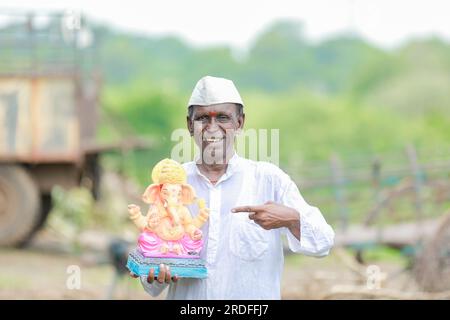 Ein alter indischer Mann, der Lord Ganesha Idol in den Händen hält, ein glücklicher, alter, armer Mann Stockfoto