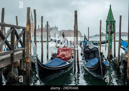 Venedig, Italien - 27. April 2019 : Ein hölzerner Pier mit einer Laterne, Gondeln und einem Gondoliere im Hintergrund in Venedig, Italien Stockfoto