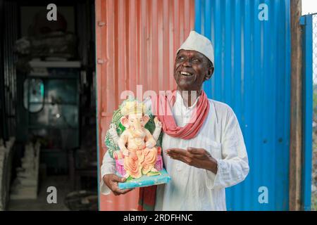 Ein alter indischer Mann, der Lord Ganesha Idol in den Händen hält, ein glücklicher, alter, armer Mann Stockfoto
