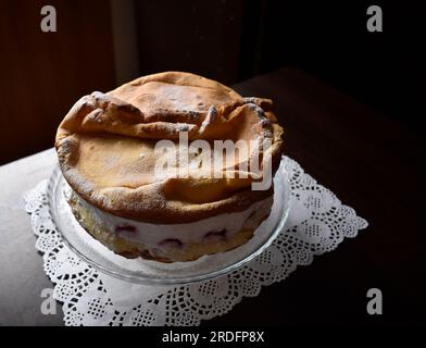 Wunderschöner und köstlicher 'Karpaten'-Kuchen mit Erdbeeren auf einem durchsichtigen Teller auf dem Holztisch mit weißer Teigmasse. Stockfoto