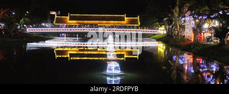 Ein Foto mit einer hell beleuchteten Brücke über einem kleinen Fluss in Siem Reap, Kambodscha, mit hellen Farben, die auf der Wasseroberfläche reflektieren. Stockfoto