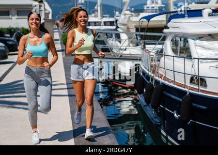 Zwei glückliche Frauen, die bei Sonnenaufgang laufen. Fröhliche, multiethnische Jogger im Freien Stockfoto