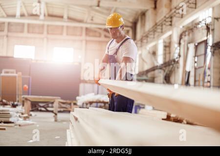 Seriöse männliche Baumeister trägt Holzbrett auf der Baustelle Stockfoto