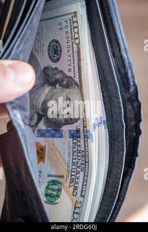 Ein Mann in einem weißen Hemd hat eine Geldbörse mit Geld, zählt sie und bietet sie einem anderen an. Nahaufnahme männliche Hand, die uns Dollar zählt und Geld hält. Der Betrug Stockfoto