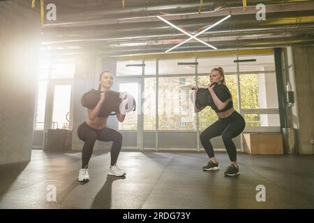 Gruppe sportlicher Frauen im Aerobic-Unterricht, die Bag-Squat-Übungen im Fitnessstudio durchführen Stockfoto