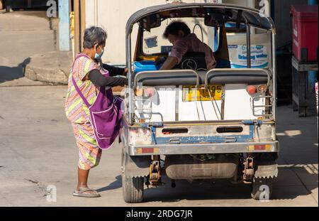 SAMUT PRAKAN, THAILAND, FEBRUAR 02 2023, eine ältere Frau in einer Schürze, ein motorisiertes dreirädriges Tuk Tuk Taxi Stockfoto