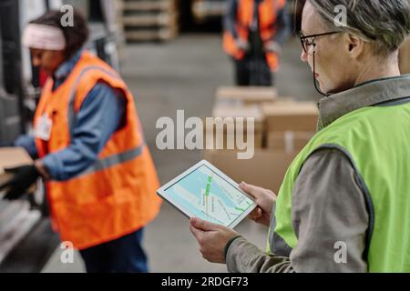 Rückansicht des Managers, der den Lieferweg auf dem digitalen Tablet während des Ladens im Lager prüft Stockfoto