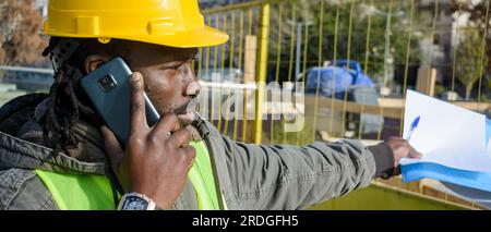 Banner eines schwarzen Bauarbeiters im gelben Sicherheitshelm, draußen telefoniert ein Problem mit dem Versicherer lösen, Kopierraum. Stockfoto