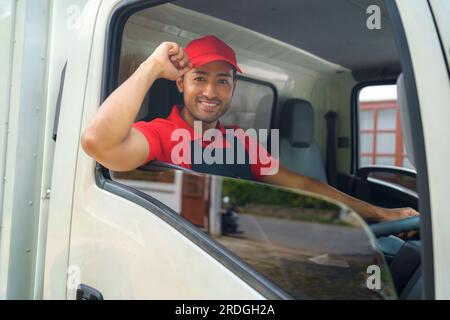 Der Transportarbeiter sitzt im Laster und lächelt vor Bereitschaft und Hingabe, während er sich auf den Weg zu einem neuen Haus macht. Ihre Begeisterung und ihr Engagement Stockfoto