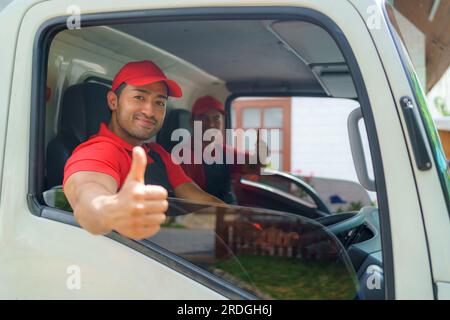 Der Transportarbeiter sitzt im Laster und lächelt vor Bereitschaft und Hingabe, während er sich auf den Weg zu einem neuen Haus macht. Ihre Begeisterung und ihr Engagement Stockfoto