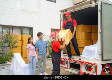 Ein asiatisches Paar steht zusammen und beobachtet mit Vorfreude, wie Arbeiter in ihr neues Zuhause ziehen. Spannung füllt die Luft, wie sie eifrig erwarten Stockfoto