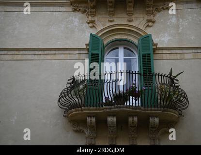 Antikes Haus mit Rokoko-Fassade mit grünen Holzfensterläden und einem handgefertigten Schmiedeeisengeländer an einer Steinmauer in Noto Sizilien, Italien. Stockfoto