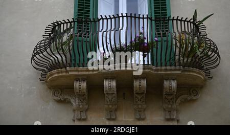 Antikes Haus mit Rokoko-Fassade mit grünen Holzfensterläden und einem handgefertigten Schmiedeeisengeländer an einer Steinmauer in Noto Sizilien, Italien. Stockfoto