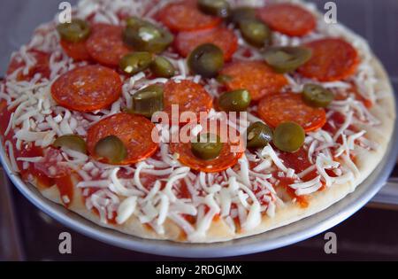 Essen, gekocht, Pizza, gefrorene Peperoni und Jalapeno-Pizza auf einem Metalltablett, fertig zum Kochen. Stockfoto