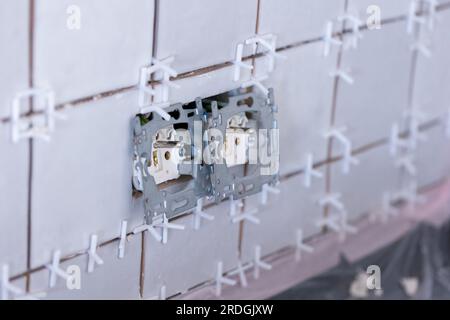 Nahaufnahme von zwei angeschlossenen Steckdosen ohne Schutzkappen in einer neu gefliesten Wand, immer noch mit dem Kunststoff-Spa mit weißem Gelenk Stockfoto