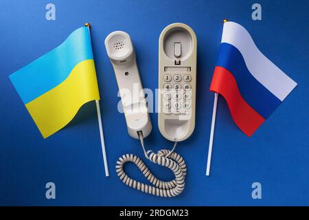 Altes Telefon und zwei Flaggen auf blauem Hintergrund, ein Konzept zum Thema Telefongespräche zwischen der Ukraine und Russland Stockfoto