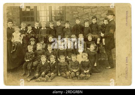 Originale charmante viktorianische Schrankkarte mit Sepia-Ton von viktorianischen Schulkindern vor einem Schulgebäude mit Schullehrern oder Lehrassistenten von Stickells & Sons, die in Cranbrook, Kent, ansässig waren. aber in Sussex und Surrey aktiv, was den Standort dieser Schule unbekannt machte, aber in Südostengland, Großbritannien, datiert 1884. Stockfoto