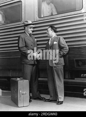 Vereinigte Staaten: ca. 1944 zwei Männer in Anzügen schütteln sich an einem Bahnhofsstand die Hände. Stockfoto