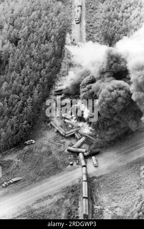 Houston, Alaska: 5. August 1972 beinahe 40 mit Benzin beladene Autos eines Güterzugs der Alaska Railroad brennen nach einer Kollision mit einem leeren Tankwagen. Der Tankteil des Lkws ist auf der Autobahn rechts neben dem Zug zu sehen, während sich die Hälfte von Fahrerhaus und Anhänger ganz links befindet. Stockfoto