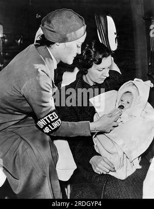 Vereinigte Staaten: c. 1947 Eine Stewardess von United Airlines gibt einem Baby eine Flasche im Flugzeug, während die Mutter zusieht. Stockfoto