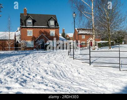 Schneebedeckte Straße mit Reifenspuren und Fußspuren auf Wohnsiedlungen in Winter, Leicestershire, England, Großbritannien Stockfoto