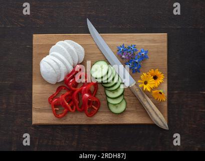 Zubereitung von Salat mit Mozarella, Paprika, Gurke und essbaren Wildblumen, Kalendula und Borretsch Stockfoto