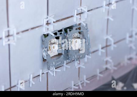 Nahaufnahme von zwei angeschlossenen Steckdosen ohne Schutzkappen in einer neu gefliesten, unfertigen Wand, immer noch mit Kunststoffweiß Stockfoto