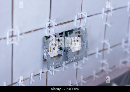 Nahaufnahme von zwei angeschlossenen Steckdosen ohne Schutzkappen in einer neu gefliesten Wand, immer noch mit dem weißen Kunststoffanschluss Spa Stockfoto