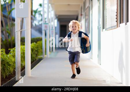 Kind, das zur Schule geht. Junge läuft in Schulhof. Kleine Schülerin freut sich, wieder in die Vorschule oder den Kindergarten. Beginn der Klasse nach dem Urlaub. Stockfoto