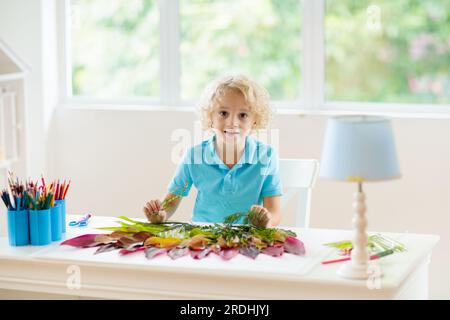 Kind schafft Bild mit bunten Blättern. Kunst und Kunsthandwerk für Kinder. Kleiner Junge, der Collagebild mit Regenbogenpflanzen-Blatt macht. Hausaufgaben für die Biologie Stockfoto