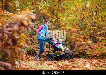 Familienwandern mit Kinderwagen im Herbstpark. Aktive Mutter, Baby und Kleinkind im Doppelwagen. Fit gesunde mutter geht mit Joggingwagen Stockfoto