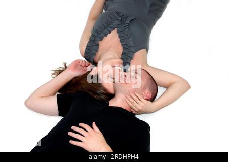 Ein hübsches Paar liegt Wange an Wange in einem weißen Raum. Ihre Augen sind geschlossen und sie berühren sich und schließen sich. Er trägt ein schwarzes Hemd und Stockfoto