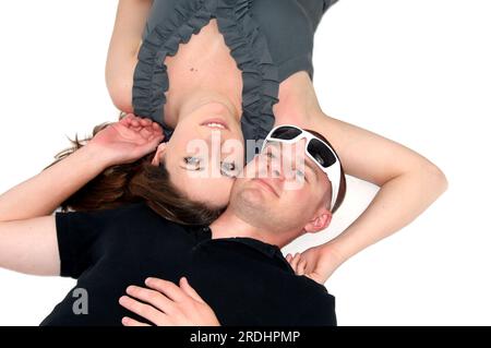 Ein Foto aus dem hohen Winkel zeigt ein Paar, das auf einem weißen Boden liegt, von Wange zu Wange. Der Mann trägt eine Sonnenbrille auf dem Kopf. Stockfoto