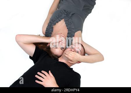Ein Paar lag in einem weißen Raum mit dicht beieinander liegenden Köpfen. Sie haben ihre Hände über den Mund des anderen und sprechen nicht. Stockfoto
