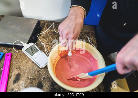 Obere Nahaufnahme der Hände des Küchenchefs Messen Sie die Temperatur der geschmolzenen Rubinschokolade in der Schüssel. Weißer Mann, der köstliches Eis zubereitet. Ein durcheinander gewordener ktchen-Hintergrund. Hochwertiges Foto Stockfoto