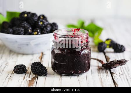 Hausgemachte Brombeerkonserven oder Marmelade in einem Maurerglas, umgeben von frischen Brombeeren aus biologischem Anbau. Selektiver Fokus mit verschwommenem Vorder- und Hintergrund. Stockfoto