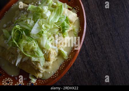 Grüne Enchiladas mit Salat serviert in einer Tonschale auf einem Holztisch. Stockfoto