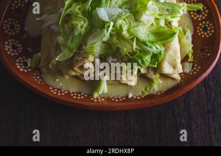 Grüne Enchiladas mit Salat serviert in einer Tonschale auf einem Holztisch. Stockfoto