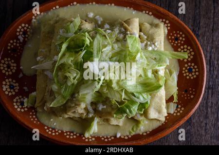 Grüne Enchiladas mit Salat serviert in einer Tonschale auf einem Holztisch. Stockfoto