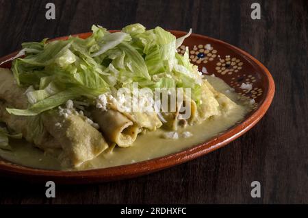 Grüne Enchiladas mit Salat serviert in einer Tonschale auf einem Holztisch. Stockfoto