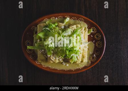 Grüne Enchiladas mit Salat serviert in einer Tonschale auf einem Holztisch. Stockfoto