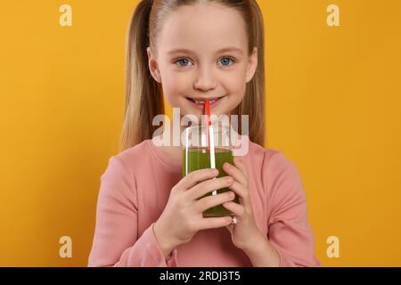 Süßes kleines Mädchen, das frischen Saft auf orangefarbenem Hintergrund trinkt Stockfoto