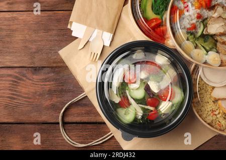 Leckeres Essen in Behältern mit Messer und Gabel auf Holztisch, flach liegend. Platz für Text Stockfoto