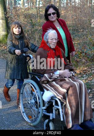 Urenkel mit Tochter, 3 Generationen, 95 Jahre alte allte Frau im Rollstuhl mit Nachkommen Stockfoto