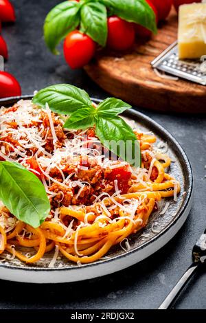 Spaghetti Bolognese oder Pasta mit Hackfleisch in Tomatensoße mit grünem Basilikum und geriebenem Parmesankäse, dunkler Tisch, Draufsicht Stockfoto