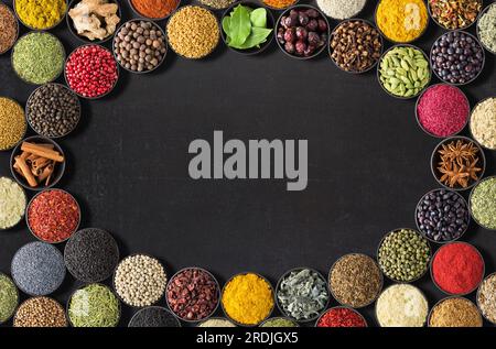 Verschiedene Gewürze liegen herum. Indische Gewürze und Kräuter auf schwarzem Tisch. Würzen mit leerem Platz für Text Stockfoto