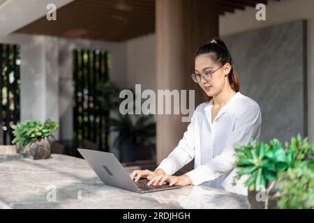 Wunderschöne junge asiatische Geschäftsfrau, die mit einem Laptop im Café sitzt. Freiberufler, der allein im Café mit einem Computer-Laptop arbeitet. Stockfoto
